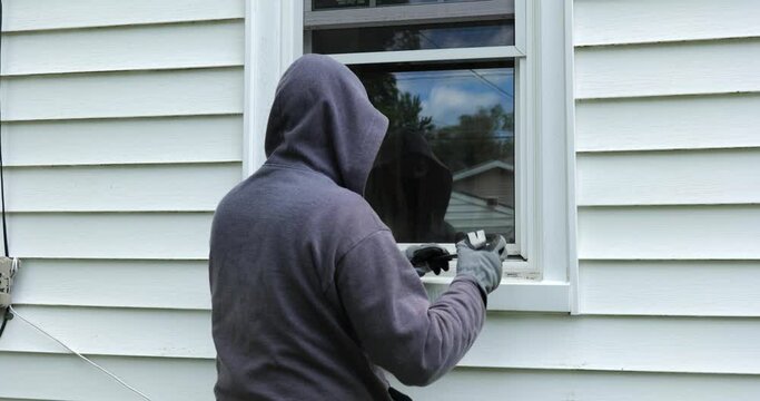 Burglar pries open a window with a crowbar and starts to climb into a home
