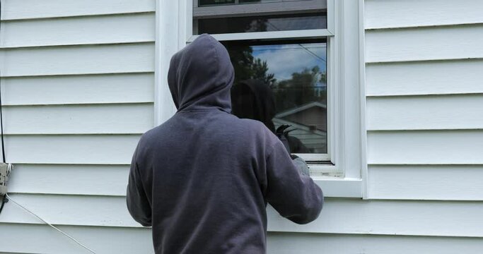 Burglar pries open a window with a crowbar and starts to climb into a home
