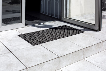 threshold made of light gray ceramic tiles with steps at the entrance to the store with a foot mat...