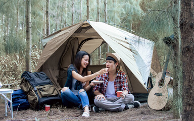 Obraz na płótnie Canvas Adorable sweet Asian adult two people or couple sitting at tent in forest for camping, smiling with happiness and freedom, eating together and enjoying adventure activity in summer vacation.