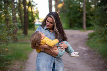 young mother is spinning with a baby in her arms. happy mom dancing with toddler on the background of nature and forest. mom and daughter laugh