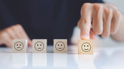 Close up of hand customer hand choose a smiley face and blurred sad face icon on the wood cube,...