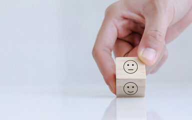 Close up of hand customer hand choose a smiley face and blurred sad face icon on the wood cube,...