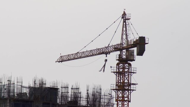 construction crane towering over a tower skyscraper high rise building under construction with rebar bars sticking out and people moving even during a rain thunder storm with clouds moving and straps