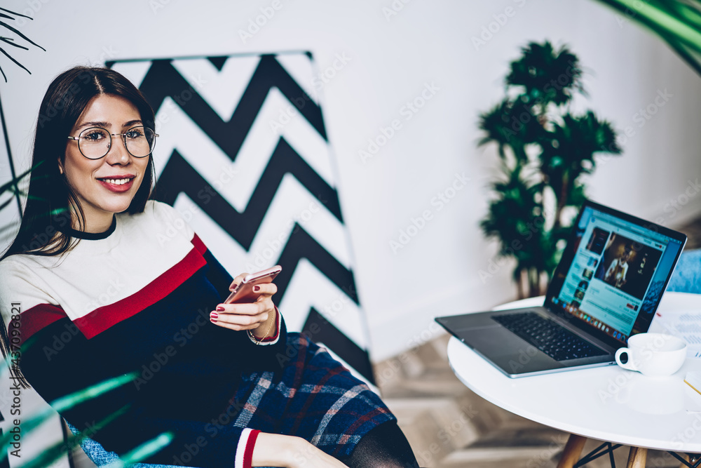 Poster portrait of happy caucaisan freelancer in classic spectacles smiling at camera while waiting for sma