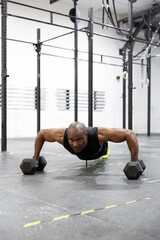 Fototapeta na wymiar African American man doing pushups with kettlebells on gym floor. Intense workout of body strength. 