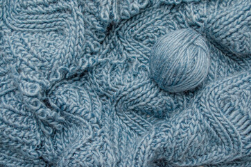 a ball of woolen threads on a handmade knitted fabric. The textured surface of a warm textile, scarf or sweater.