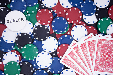 Jetons de casino en fond avec un jeton de dealer et des cartes de poker au premier plan