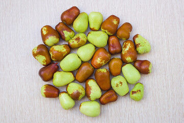 Brown and green dates with water droplets on a light wood background. The fruits are laid out in a circle. 32 dates. View from above. Image for texture, background.