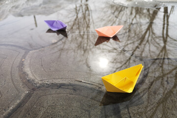 Paper boats in the spring in a puddle of water with reflections of trees. The concept of success, career advancement. Origami, children's creativity.