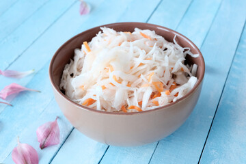 Pickled cabbage with carrots in a deep clay round gray bowl. Blue boards background. Snacks, pickles