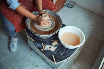Young woman ceramist throwing clay pot on pottery wheel
