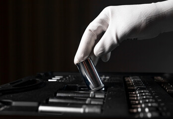 Male hand close up in white glove over open toolkit with metal tools for car and home repair, head.