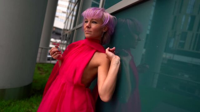 portrait of a woman in a bright dress and with pink hair. she leaned against the mirrored wall. the camera is moving
