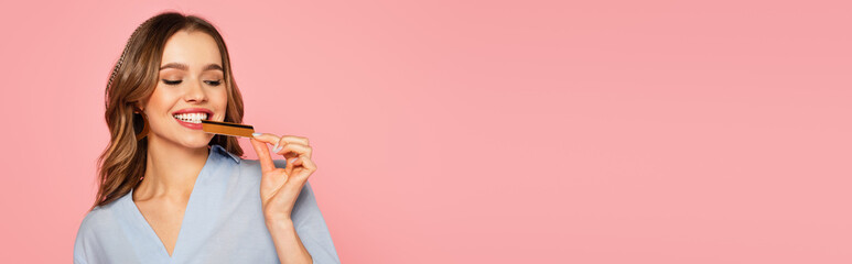Smiling woman biting credit card isolated on pink, banner
