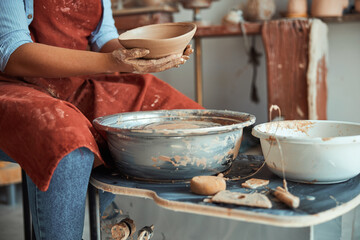 Female potter in apron holding earthenware bowl