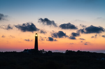 Lighthouse in the dunes and clouds during sunset.