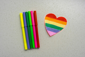 heart painted in rainbow colors of the lgbt community and multicolored markers on a table. heart in...