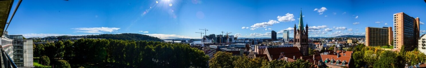 Fototapeta premium Summertime panorama of blue sky, cityscape and forest