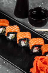 A set of sushi rolls Philadelphia with red fish, cream cheese and black rise lies in a plate boat. Sushi rolls on a gray background
