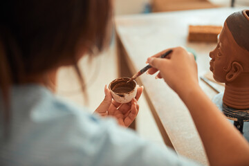 Young woman holding paintbrush and bowl with brown paint
