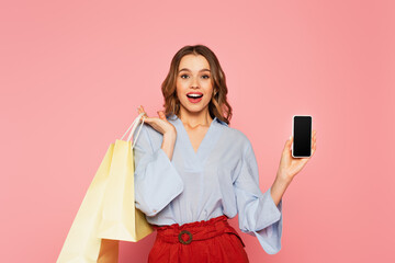 Fototapeta na wymiar Pretty woman with shopping bags and smartphone looking at camera on pink background
