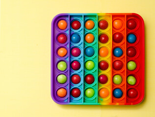New popular silicone colorful antistress pop it toy for child on yellow background. View from above. Copy space. Simple dimple