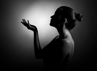 A silhouette of a beautiful young woman in profile with her palm outstretched against a dark background.