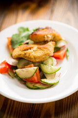 fried chicken fillet with fresh cucumbers, tomatoes and radishes in a plate
