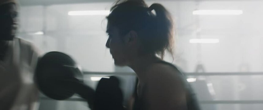 HANDHELD CU Portrait of Caucasian female boxer practicing punches with her coach on a boxing ring. Shot with 2x anamorphic lens