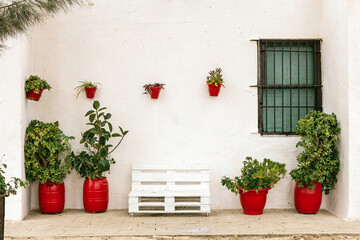 Beautiful white facade of a typical Andalusian house in Spain with plants in red clay pots - obrazy, fototapety, plakaty