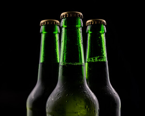 Three bottles of beer from green glass on black background.
