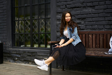 Pretty Caucaisan tourist dressed in trendy denim apparel and skirt resting at street bench and...