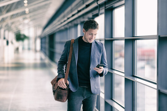 Mobile phone business man walking in airport with messenger bag using cellphone texting sms message on smartphone app - businesspeople commute lifestyle. Young professional businessman.