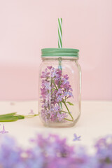 Lilac and purple flowers in a smoothie jar on a yellow background Concept, summer heat, quench...