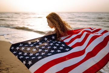 Young woman with american flag on the beach at sunset. 4th of July. Independence Day. Patriotic holiday. - Powered by Adobe