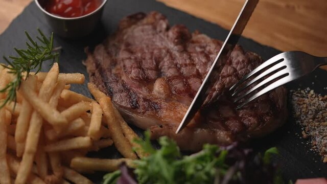 cutting steak with knife and fork on black plate, slow motion 4k 120p