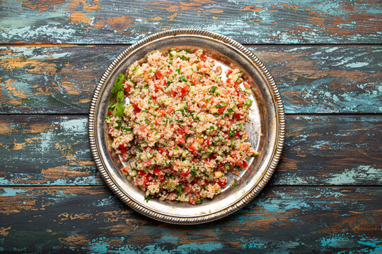 Middle eastern and Mediterranean traditional vegetable salad tabbouleh with couscous on rustic metal plate and wooden background from above. Arab Turkish food
