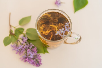 Lilac, purple flowers in a glass with tea on a yellow modern background. Concept, heat, quench your...