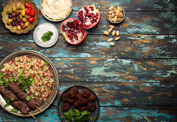 Various Turkish dishes: meat kebab with tabbouleh salad, falafel, hummus, olives, pistachios and Middle Eastern meze on wooden table top view with copy space. Ethnic arab food, cuisine of Turkey