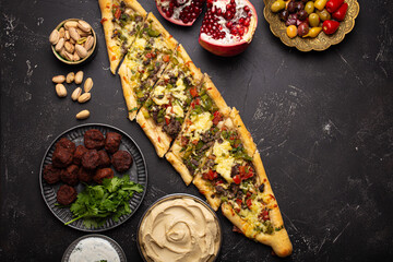 Various Turkish dishes: pide pizza, meat kebab with tabbouleh salad, falafel, hummus, olives and Middle Eastern meze on black table top view with copy space. Ethnic arab food, cuisine of Turkey - obrazy, fototapety, plakaty