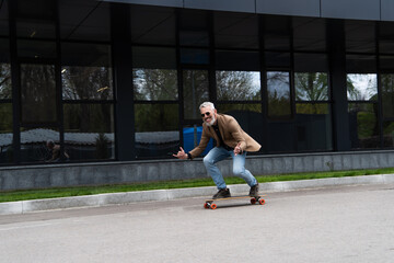 full length of happy middle aged man in sunglasses riding longboard and gesturing outside