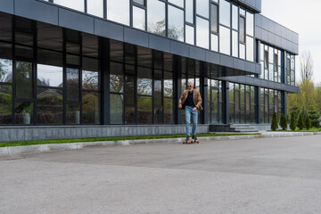 full length of bearded and mature man in sunglasses riding longboard outside