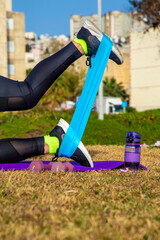 female legs in sportswear are doing exercises with blue sports elastic band outdoor. Sports, yoga,...