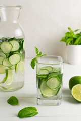 A glass of detox water infused with cucumber and mint, with a jug and ingredients. Health care, fitness, healthy food concept.