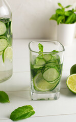 A glass of detox water infused with cucumber and mint, with a jug and ingredients. Health care, fitness, healthy food concept.