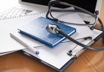 Stethoscope, computer, notebook and pen on wooden background. Doctors desk.