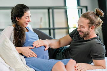 Obraz premium Pregnant woman lie on bed and her husband touch belly and smile in bedroom. Concept of happy family stay at home with love relationship.