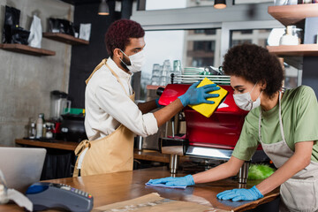 Fototapeta premium African american baristas in medical masks cleaning bar and coffee machine in cafe