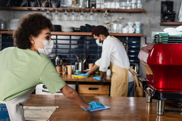 African american barista in medical mask cleaning bar near coffee machine